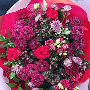 Hand-tied bouquet of red and pink roses, deep pink chrysanthemums and astrantia in red and pink wrap