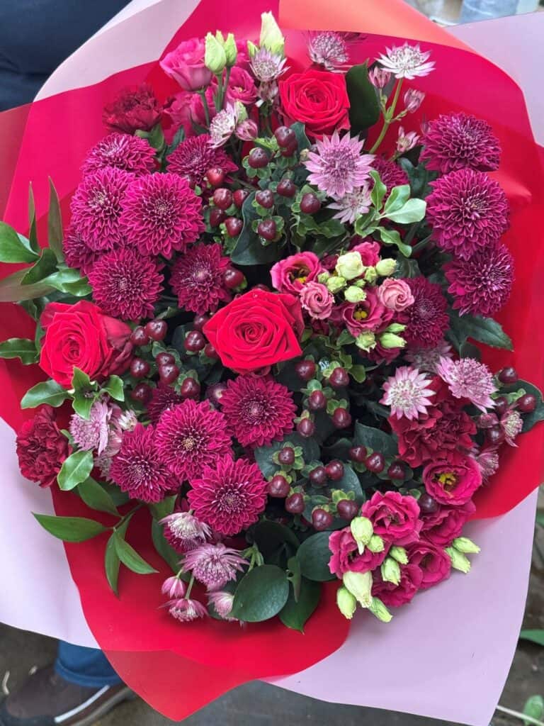 Hand-tied bouquet of red and pink roses, deep pink chrysanthemums and astrantia in red and pink wrap