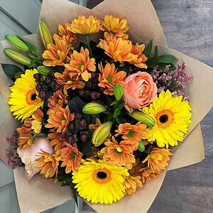 Autumn bouquet of orange chrysanthemums, yellow gerberas and a peach rose in kraft paper