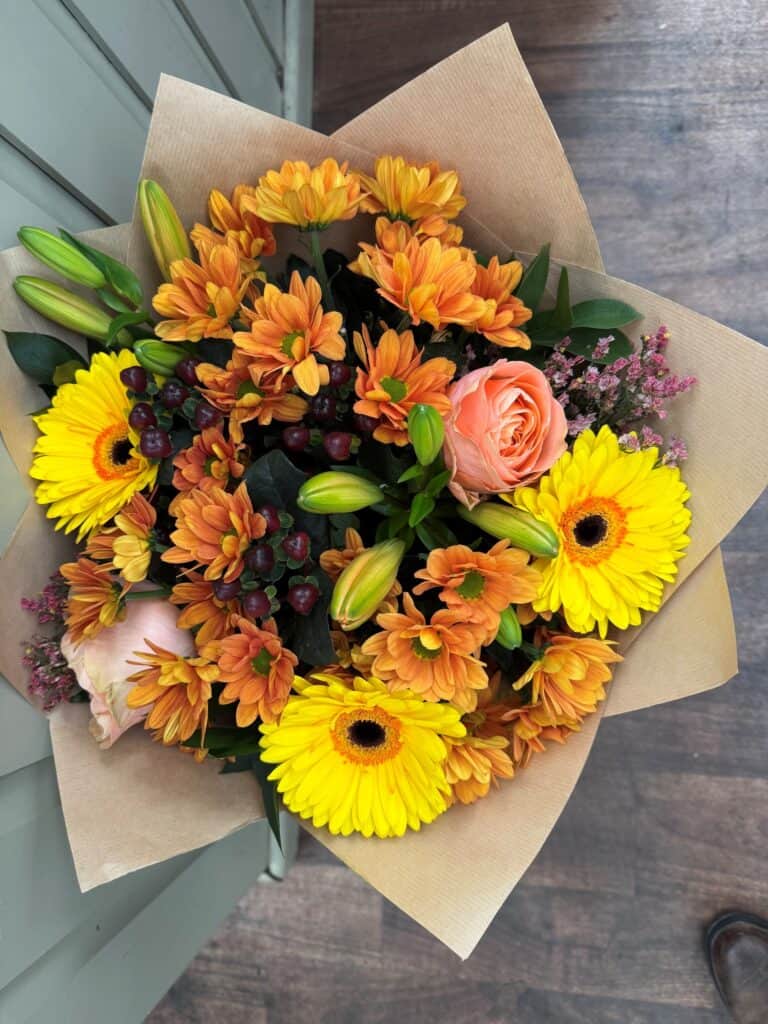 Autumn bouquet of orange chrysanthemums, yellow gerberas and a peach rose in kraft paper